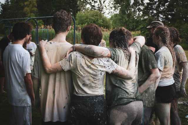 muddy children with their arms around each other with their backs to the camera